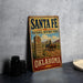 A vintage-style sign for the Santa Fe National Historic Trail in Oklahoma, featuring a wagon train and desert landscape.