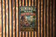 A metal sign with the text "SEMINOLLE WARS HERITAGE TRAIL" and "FLORIDA" printed on it, hanging on a wooden wall.
