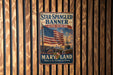 A vintage metal sign with the text "Star-Spangled Banner" and "National Historic Trail" hangs on a wooden wall.