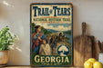 A vintage-style metal sign for the Trail of Tears National Historic Trail in Georgia, featuring an illustration of a group of people on a wagon train crossing a river.