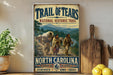 a vintage-style metal sign with a painting of a group of people traveling on a wagon, set against a scenic landscape. The sign is titled "Trail of Tears" and is located in North Carolina.