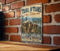 A vintage-style metal sign for the Trail of Tears National Historic Trail, featuring a historical illustration of a group of people traveling through a mountainous landscape.