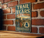A vintage-style metal sign for the Trail of Tears, a historic trail in Tennessee, is displayed on a brick wall.