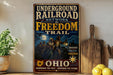 a vintage-style sign with the text "UNDERGROUND RAILROAD NETWORK TO FREEDOM TRAIL" and a depiction of a group of people on a trail. The sign is displayed on a shelf next to a wooden cutting board and a potted plant.