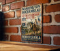 A vintage-style metal sign with the text "WASHINGTON-ROCCHAMBEAU REVOLUTIONARY ROUTE" and images of two men on horseback, mounted on a brick wall.