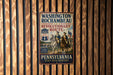 A vintage-style metal sign with the text "WASHINGTON-ROCCHAMBEAU REVOLUTIONARY ROUTE" and "PENNSYLVANIA STEP INTO HISTORY" is displayed on a wooden wall.