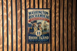 A vintage-style metal sign with the text "WASHINGTON-ROCCHAMBEAU REVOLUTIONARY ROUTE" and "RHODE ISLAND" is displayed on a wooden wall.