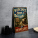 A vintage-style metal sign for the Wilderness Road in Tennessee, featuring a wagon train and a scenic landscape.