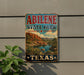 A vintage-style sign for Abilene State Park in Texas, featuring a scenic landscape with mountains, cacti, and a river.