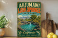 A vintage-style sign for Ahjumawi Lava Springs State Park in California, featuring a scenic image of the park's natural landscape and a mountain backdrop.