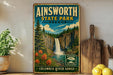 a vintage-style sign for Ainsworth State Park in Oregon, depicting a waterfall surrounded by lush greenery and colorful flowers.