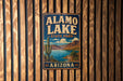 A vintage-style metal sign for Alamo Lake State Park in Arizona, featuring a desert landscape with a cactus and a lake.