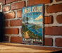 A vintage-style metal sign for Angel Island State Park in California, featuring a scenic illustration of the island and its surrounding landscape.