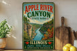 A vintage-style sign for Apple River Canyon State Park in Illinois, featuring a scenic illustration of the canyon and a message encouraging exploration, relaxation, and adventure.