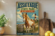 A vintage metal sign forASSATTEAGUE STATE PARK, MARYLAND, featuring a brown and white horse in a grassy field with a lighthouse in the background.