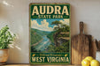 a vintage-style sign for Audra State Park, with a scenic landscape of a river and mountains in the background.