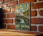 A vintage-style metal sign for Babcock State Park, featuring a scenic illustration of a waterfall and a wooden building, mounted on a brick wall.