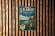A vintage-style metal sign for Backbone State Park in Iowa, featuring a scenic landscape with a cliff overlooking a river.