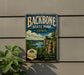 A vintage-style metal sign for Backbone State Park in Iowa, featuring a scenic landscape with a cliff overlooking a river.