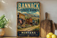 A vintage-style metal sign for Bannack State Park in Montana, featuring a scenic illustration of a small town with a dirt road, buildings, and mountains in the background.