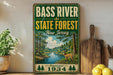 A vintage-style metal sign for the Bass River State Forest in New Jersey, featuring a scenic illustration of a deer in the foreground and a river in the background.
