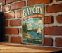 A vintage metal sign for the Bay City State Recreation Area in Michigan, featuring a scenic illustration of a lake, sailboat, and city skyline.