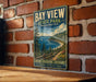 A vintage-style metal sign for Bay View State Park in Washington, featuring a scenic landscape with a lake, mountains, and pine trees.