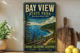 A vintage-style metal sign for Bay View State Park in Washington, featuring a scenic landscape with a lake, mountains, and pine trees.