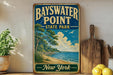 A vintage-style metal sign for Bayswater Point State Park in New York, featuring a scenic beach landscape with trees, grass, and a body of water.