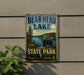 A metal sign with the text "BEAR HEAD LAKE STATE PARK MINNESOTA" and an illustration of a bear in a forest setting.