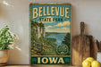 A vintage-style metal sign for Bellevue State Park in Iowa, featuring a scenic landscape with a river, cliffs, and a wooden fence.