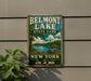 A vintage-style metal sign for Belmont Lake State Park, featuring a scenic image of the lake and surrounding landscape, with the text "Belmont Lake State Park" and "New York" prominently displayed.