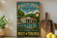 A vintage-style metal sign for Berkeley Springs State Park, featuring an illustration of the park's buildings and a clock, with a scenic view of the park and a lake.
