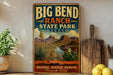 A vintage-style sign for Big Bend Ranch State Park in Texas, featuring a desert landscape with mountains, cacti, and a river.