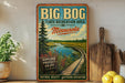 A vintage-style sign for the Big Bog State Recreation Area in Minnesota, featuring a scenic image of a wooden boardwalk leading to a lake surrounded by pine trees.