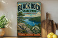 A vintage-style sign for Black Rock State Park in Connecticut, featuring a scenic landscape with a river, mountains, and a sailboat.