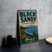 A vintage-style sign for Black Sandy State Park in Montana, featuring a scenic landscape with a lake, mountains, and pine trees.