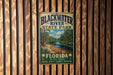 A vintage-style metal sign for Blackwater River State Park in Florida, featuring a scenic image of the river surrounded by lush greenery.