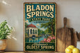 A vintage-style sign for Bladen Springs State Park in Alabama, featuring a scenic illustration of the park's landmark, Bladen Springs, with a waterfall and lush greenery.
