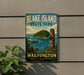 A vintage-style sign for Blake Island State Park in Washington, featuring a scenic image of the park and a boat on the water.