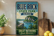 A vintage-style sign for Blue Rock State Park in Ohio, featuring a scenic landscape with a lake and mountains.