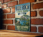 A vintage-style sign for Blue Rock State Park in Ohio, featuring a scenic landscape with a lake and mountains.