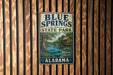 A vintage metal sign for Blue Springs State Park in Alabama, featuring a scenic illustration of a river, trees, and a wooden cabin.