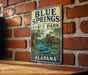 A vintage metal sign for Blue Springs State Park in Alabama, featuring a scenic illustration of the park's natural surroundings.