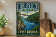 A vintage-style sign for Bluestone State Park in West Virginia, featuring a scenic image of a bridge over a river surrounded by lush greenery.
