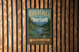 A vintage-style metal sign for Bogachiel State Park in Washington, featuring a scenic mountain landscape with a river and pine trees.