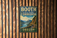 A vintage-style metal sign for the Booth State Scenic Corridor in Oregon, featuring a scenic mountain landscape with a winding road.