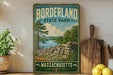 A vintage-style sign for Borderland State Park in Massachusetts, featuring a scenic landscape with a lake, trees, and a stone wall.
