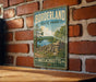 A vintage metal sign for Borderland State Park in Massachusetts, featuring a scenic landscape with a lake, trees, and a stone wall.