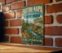 A vintage metal sign for Bothe-Napa Valley State Park in California, featuring a scenic illustration of a river and a wooden cabin.